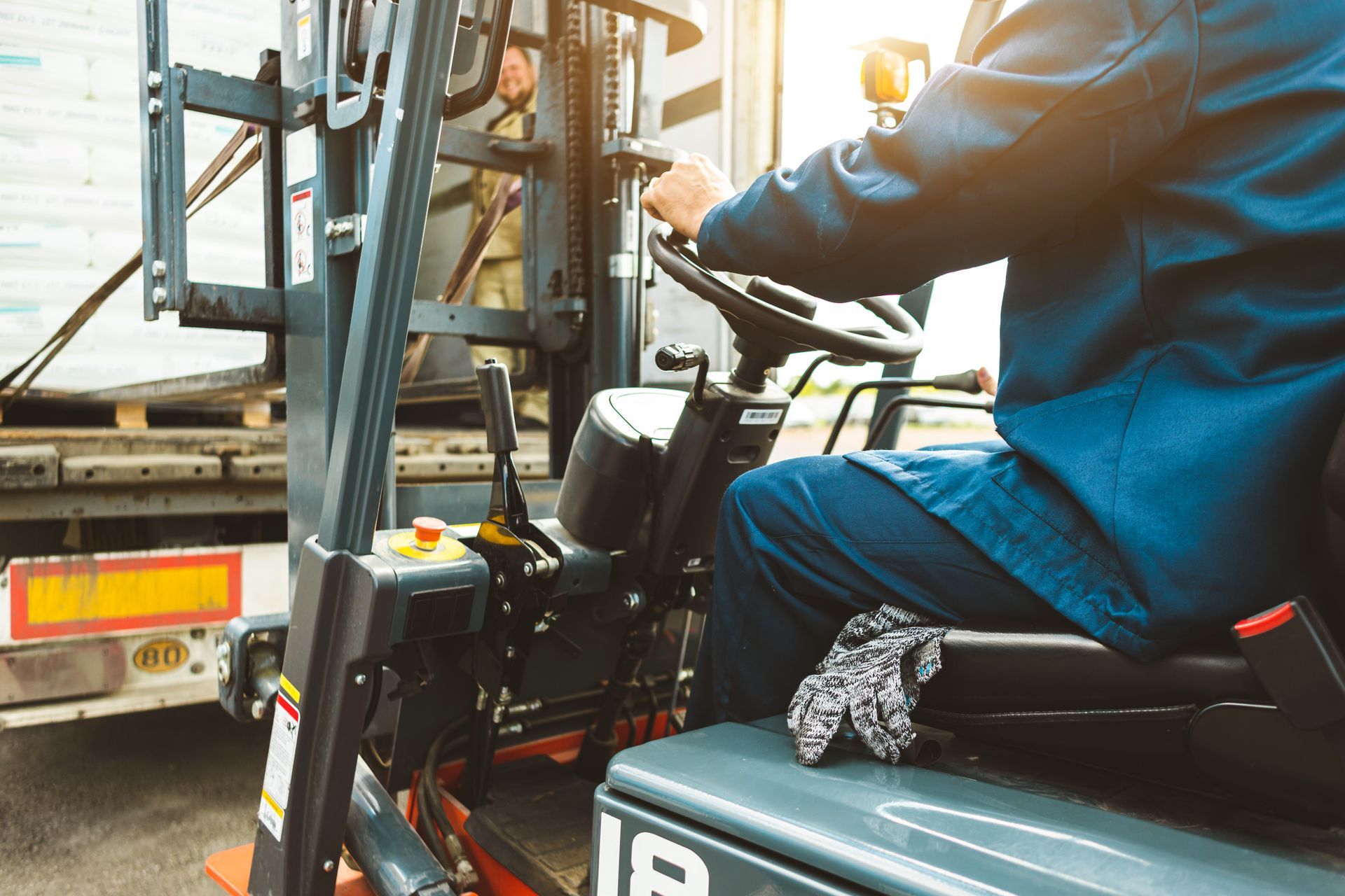 Warehouse worker operates a forklift to unload palletized goods from a truck.