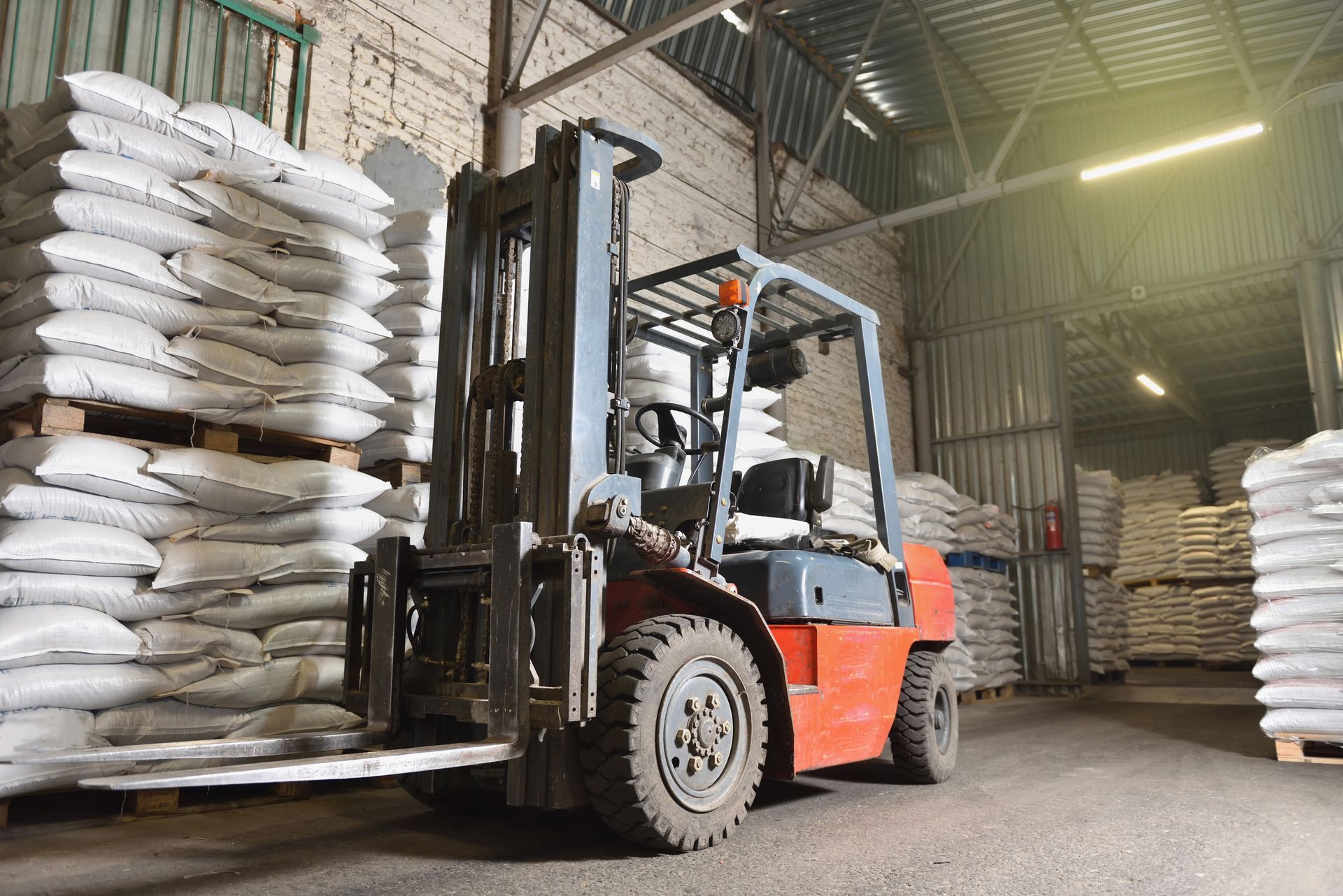 Forklift operator moving wooden pallets in a storage yard under a blue sky.