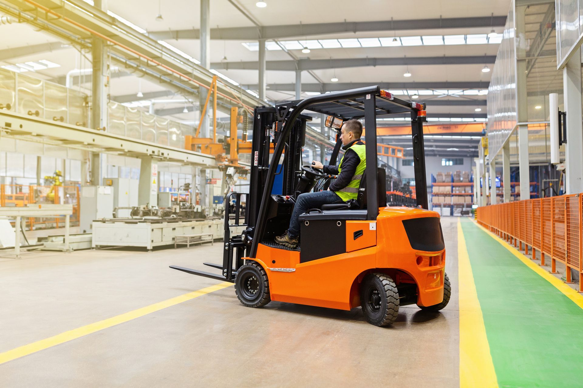 Orange forklift with driver in a factory setting.