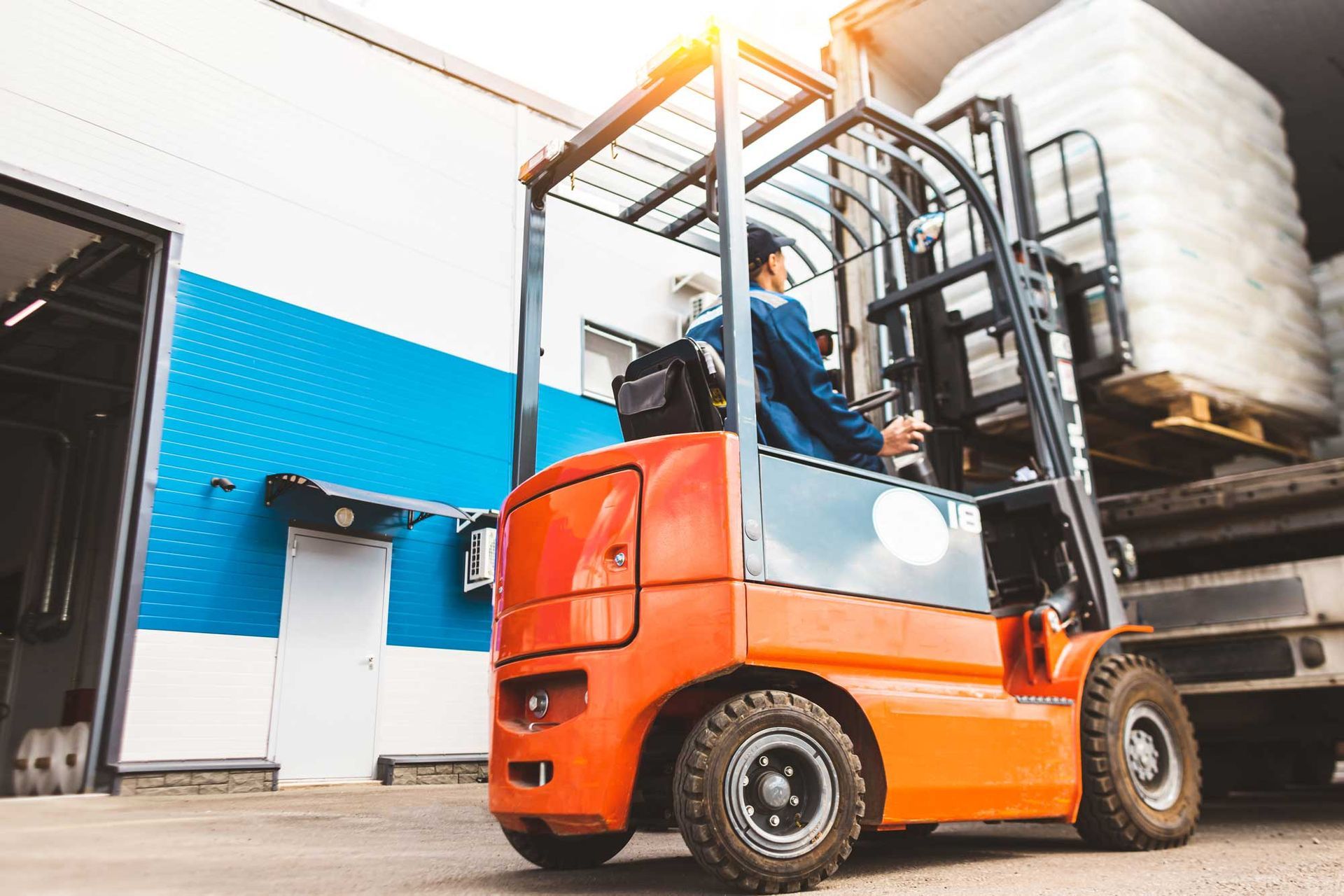 Orange forklift unloading cargo from a truck at a warehouse. Orange forklift unloading cargo from a truck at a warehouse.