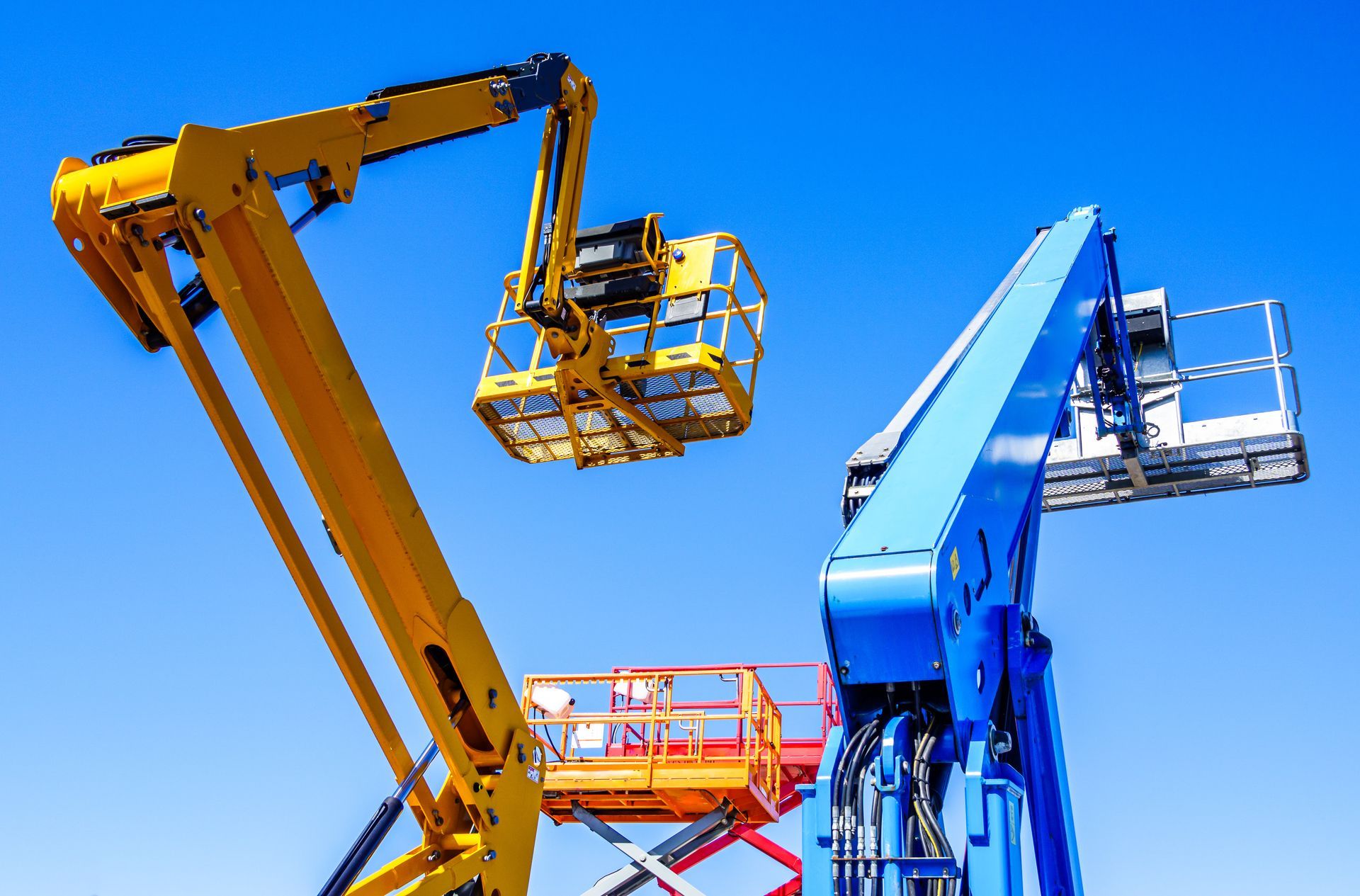 Telescoping and articulating boom lifts against a clear blue sky