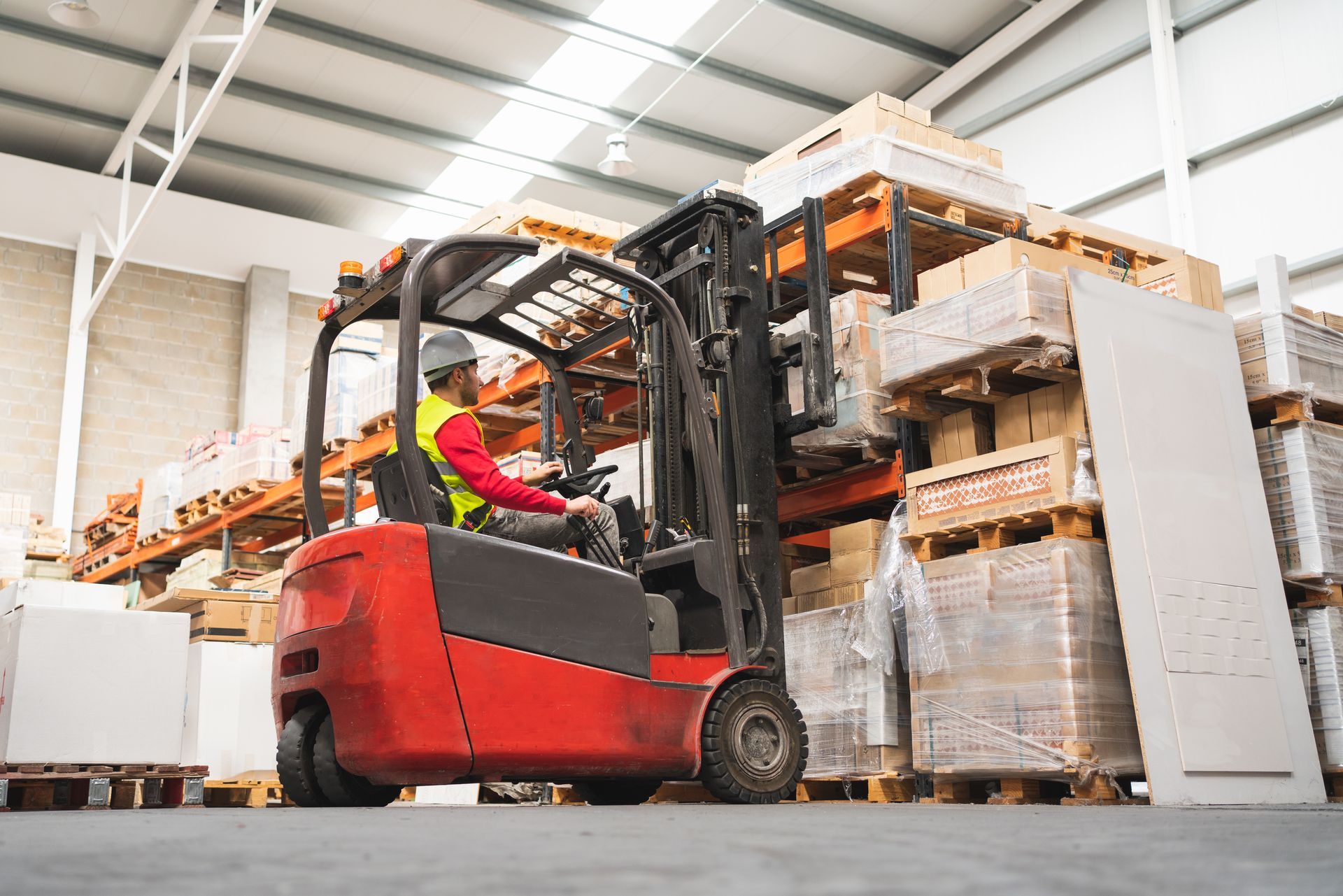 Red forklift in warehouse, lifting pallets. Driver in safety vest and helmet. Red forklift in warehouse, lifting pallets. Driver in safety vest and helmet.