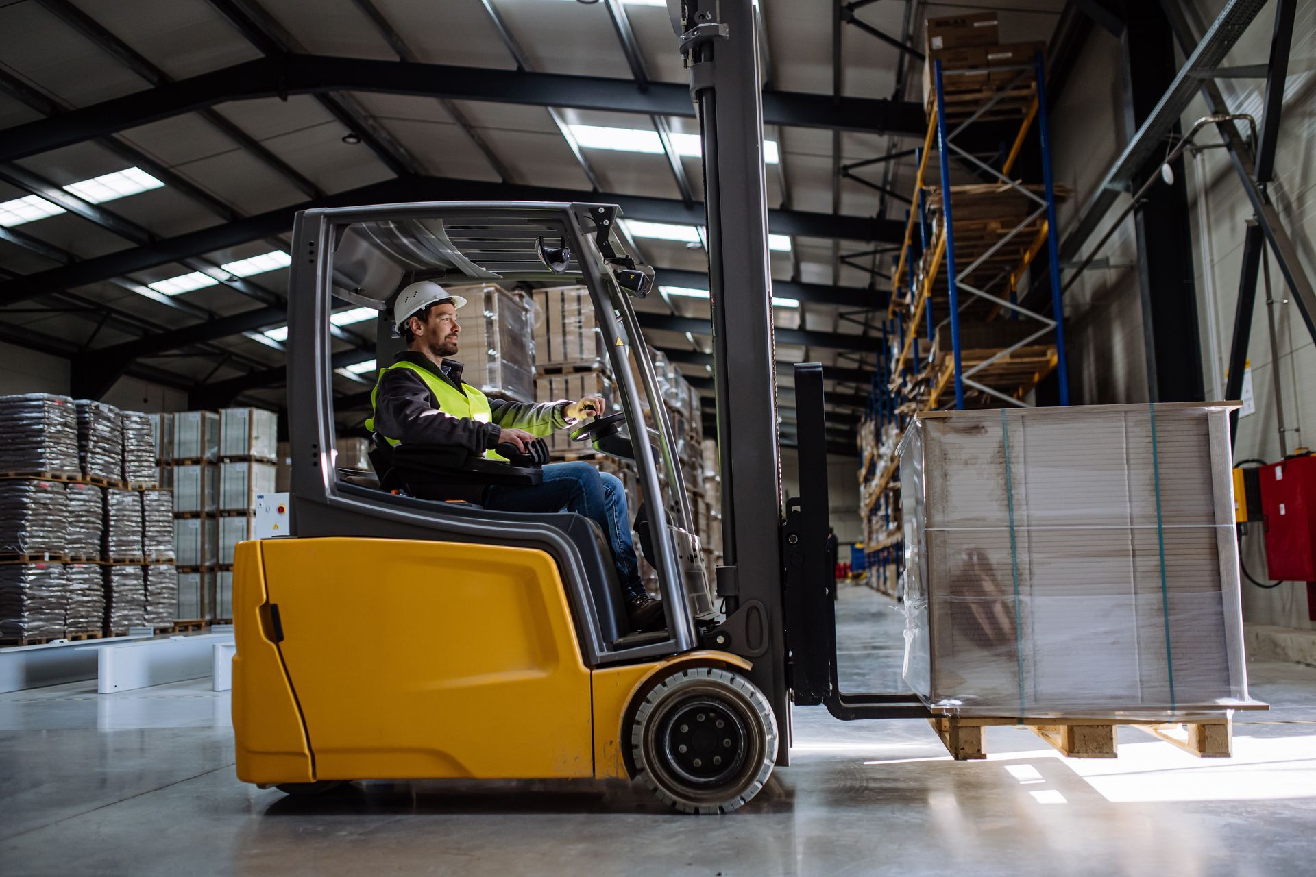 Warehouse worker operating a yellow forklift, transporting a pallet of goods.