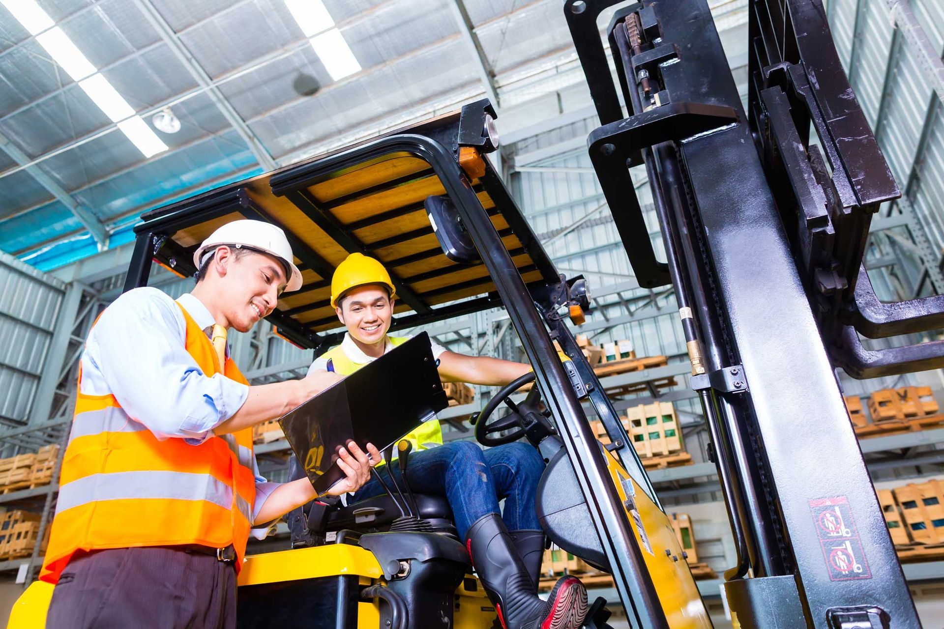 Technicians inspecting forklift parts during maintenance check inside a warehouse with safety gear. Technicians inspecting forklift parts during maintenance check inside a warehouse with safety gear.