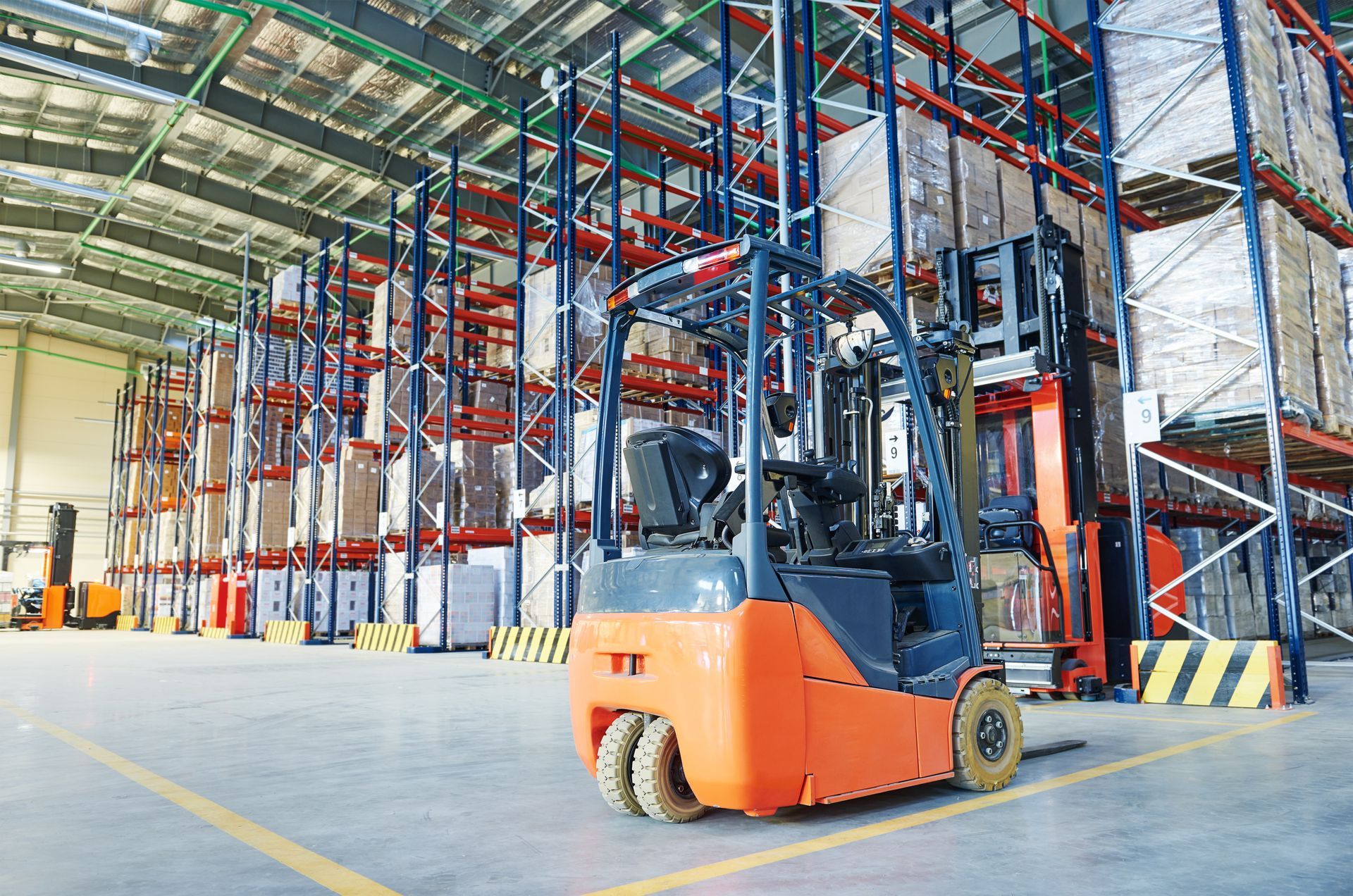 Orange forklift in a warehouse with tall shelves of packaged goods.