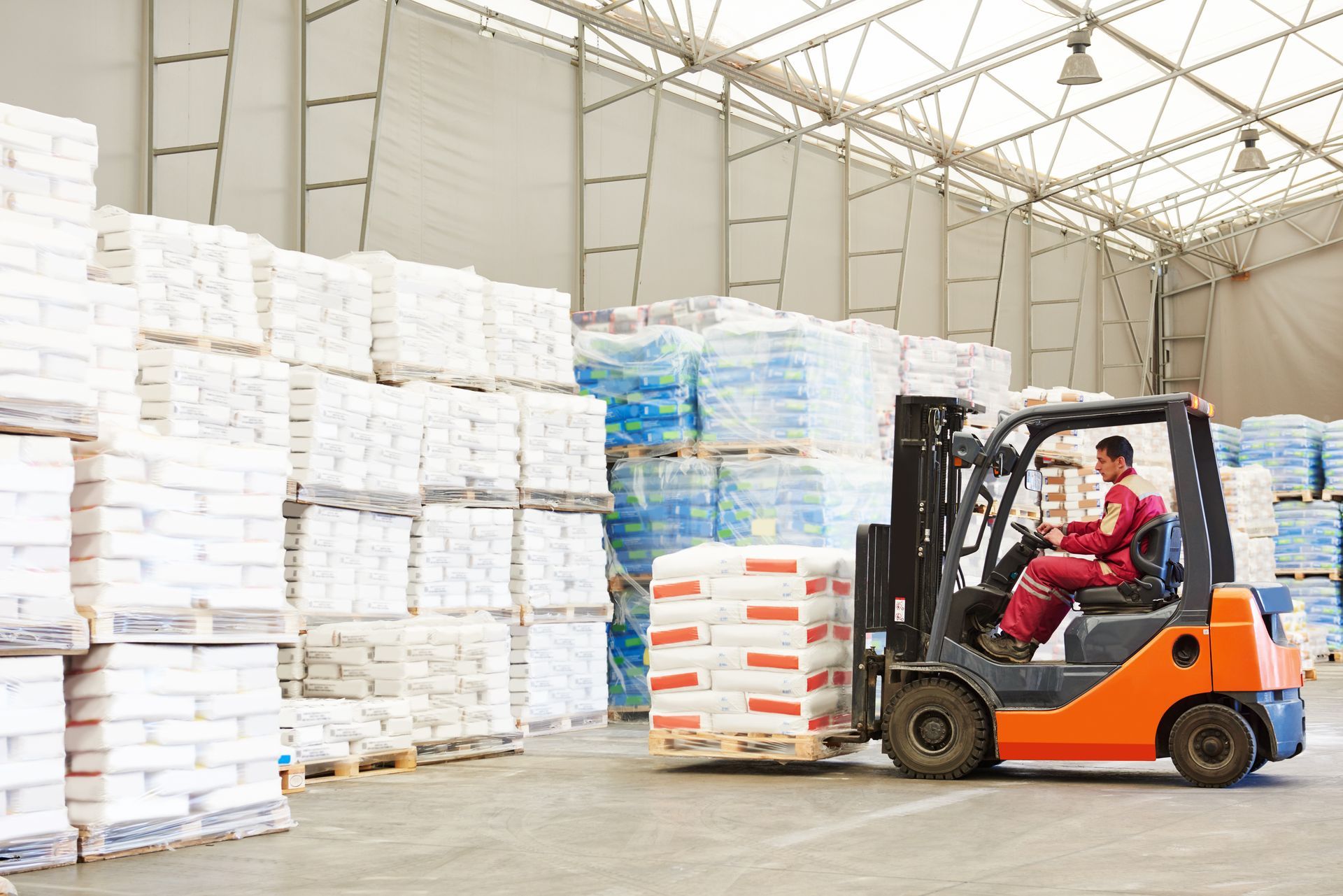 Forklift operator in a warehouse moves pallets of bagged product.