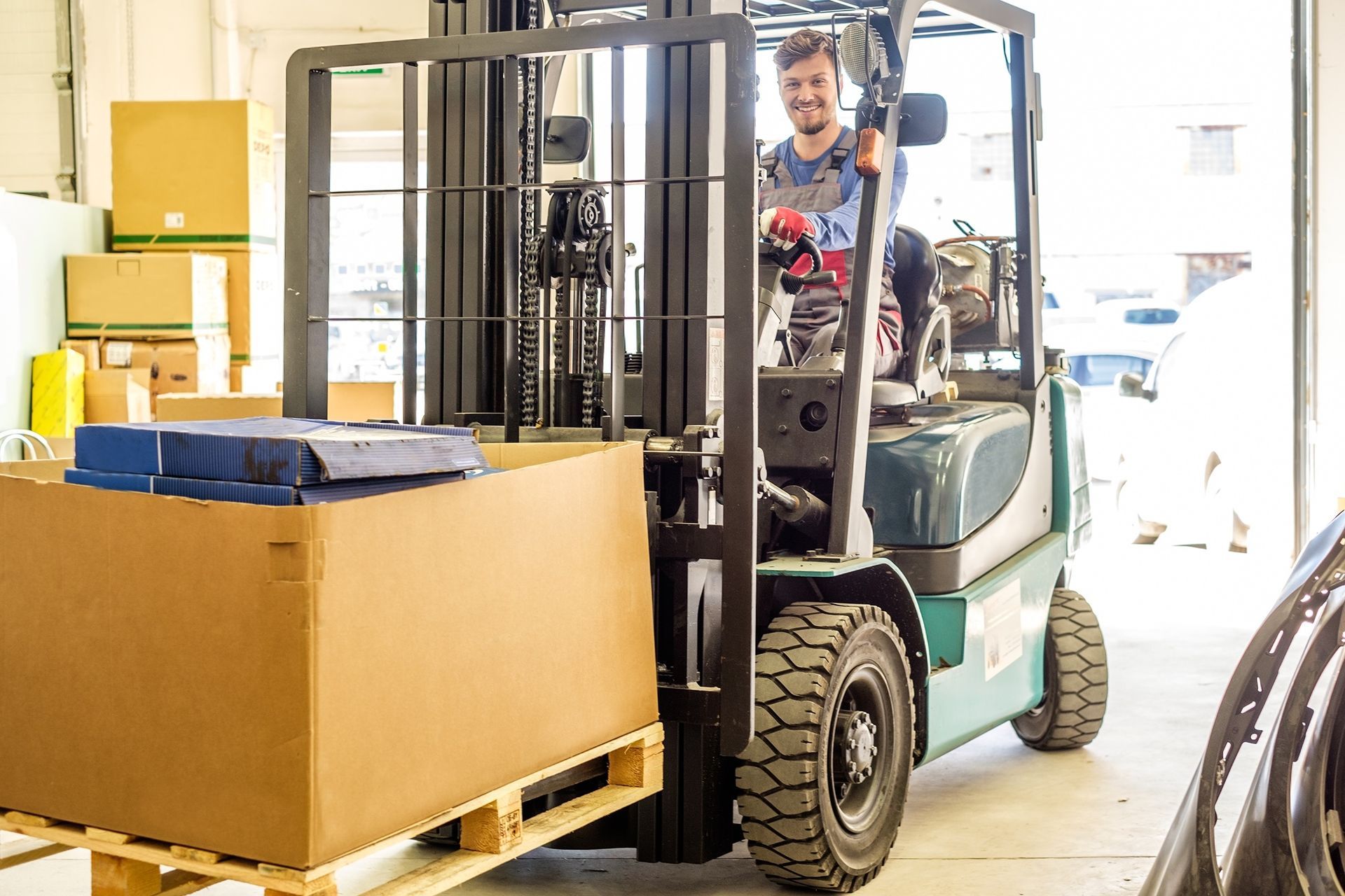 Man operating a forklift, carrying a pallet with a large cardboard box inside a warehouse. Man operating a forklift, carrying a pallet with a large cardboard box inside a warehouse.
