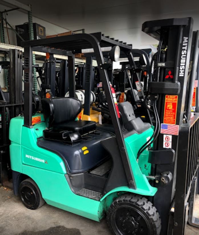 An orange forklift in a warehouse. Other forklifts are visible in the background against a concrete wall.