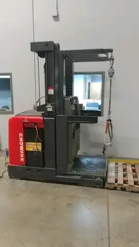 Red and black Raymond reach truck parked indoors near a loading dock and a pallet.