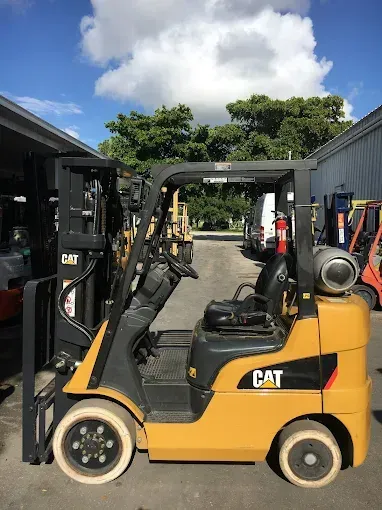 Yellow CAT forklift parked outside under a cloudy blue sky.