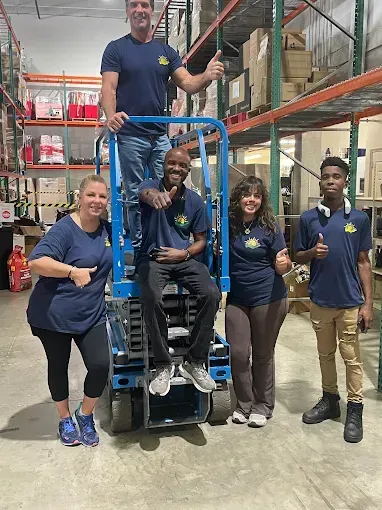 Forklift operator moving wooden pallets in a storage yard under a blue sky.