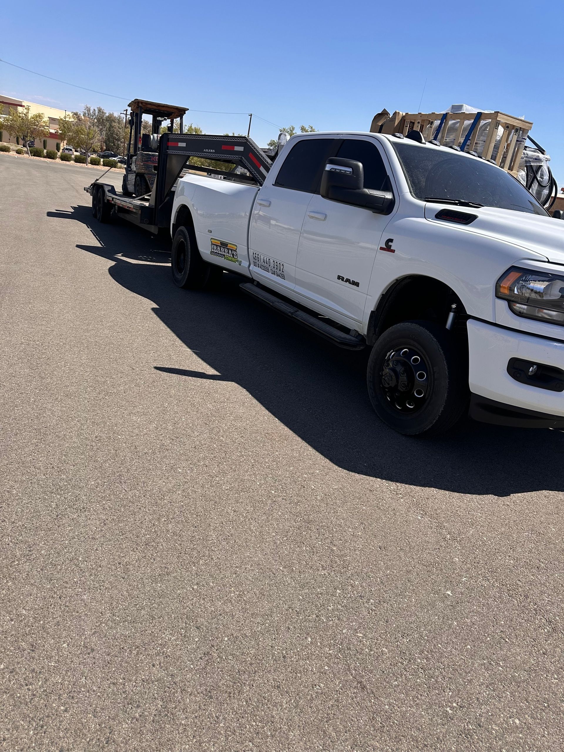 White pickup truck towing a flatbed trailer with a small tractor on it. Sunny day.