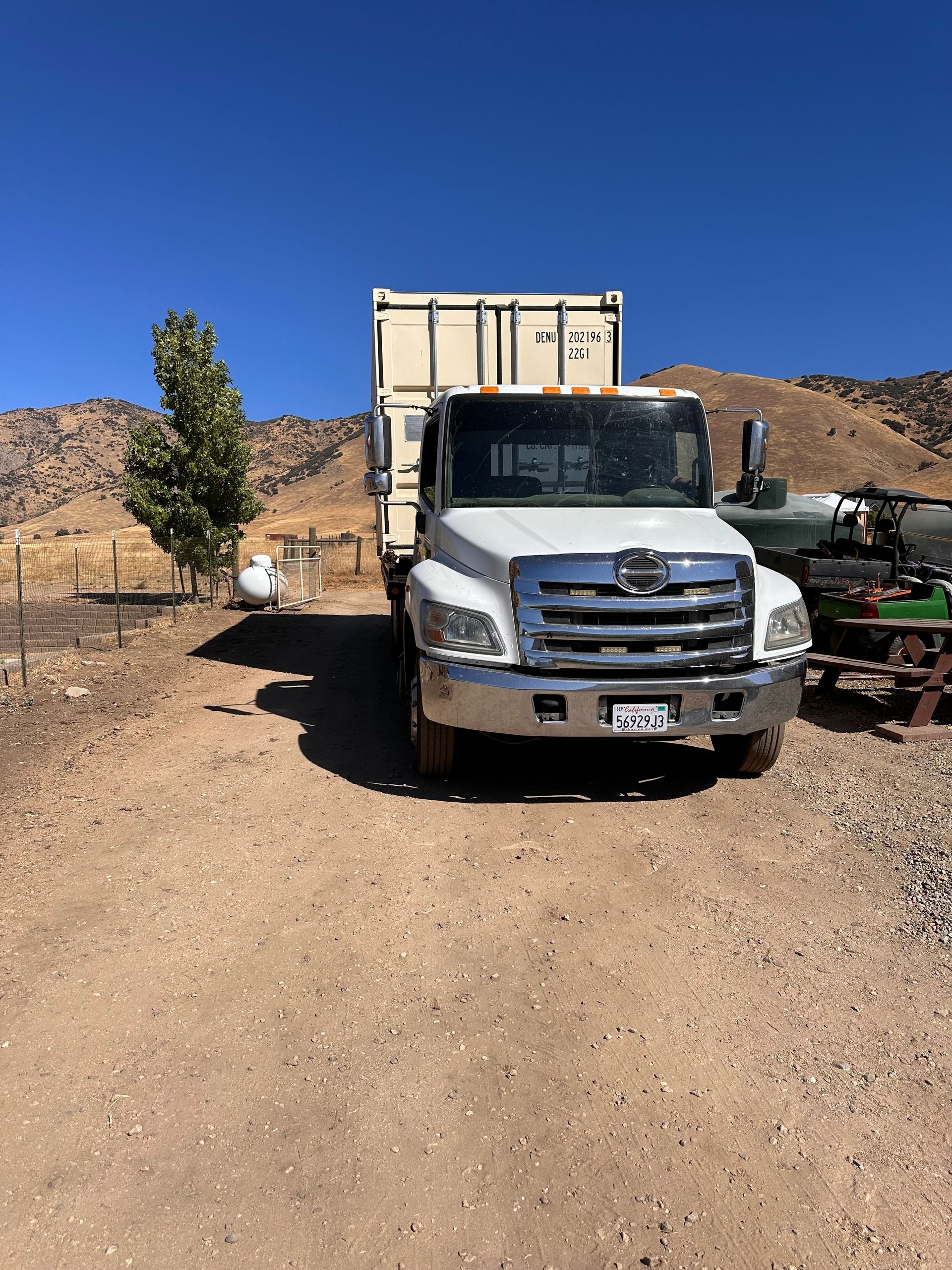 White truck with a container in a dirt field, under a blue sky.