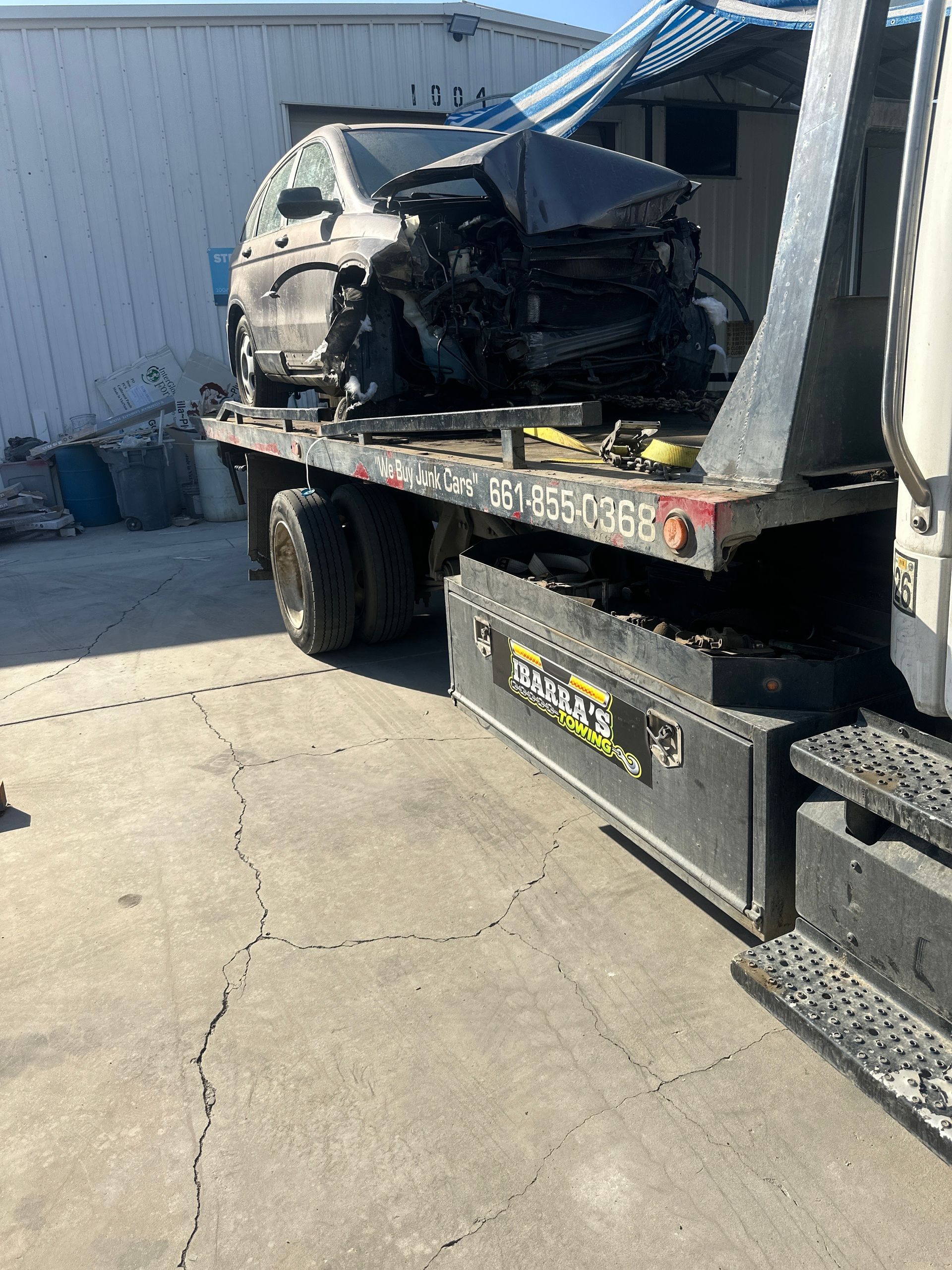 A severely damaged car loaded onto a tow truck bed in a sunlit area.