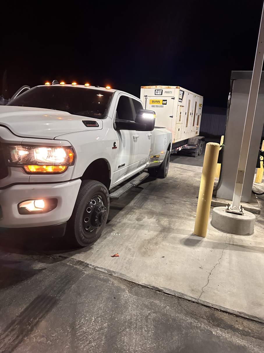 White pickup truck towing a generator trailer at night. The truck is parked at a gas station.