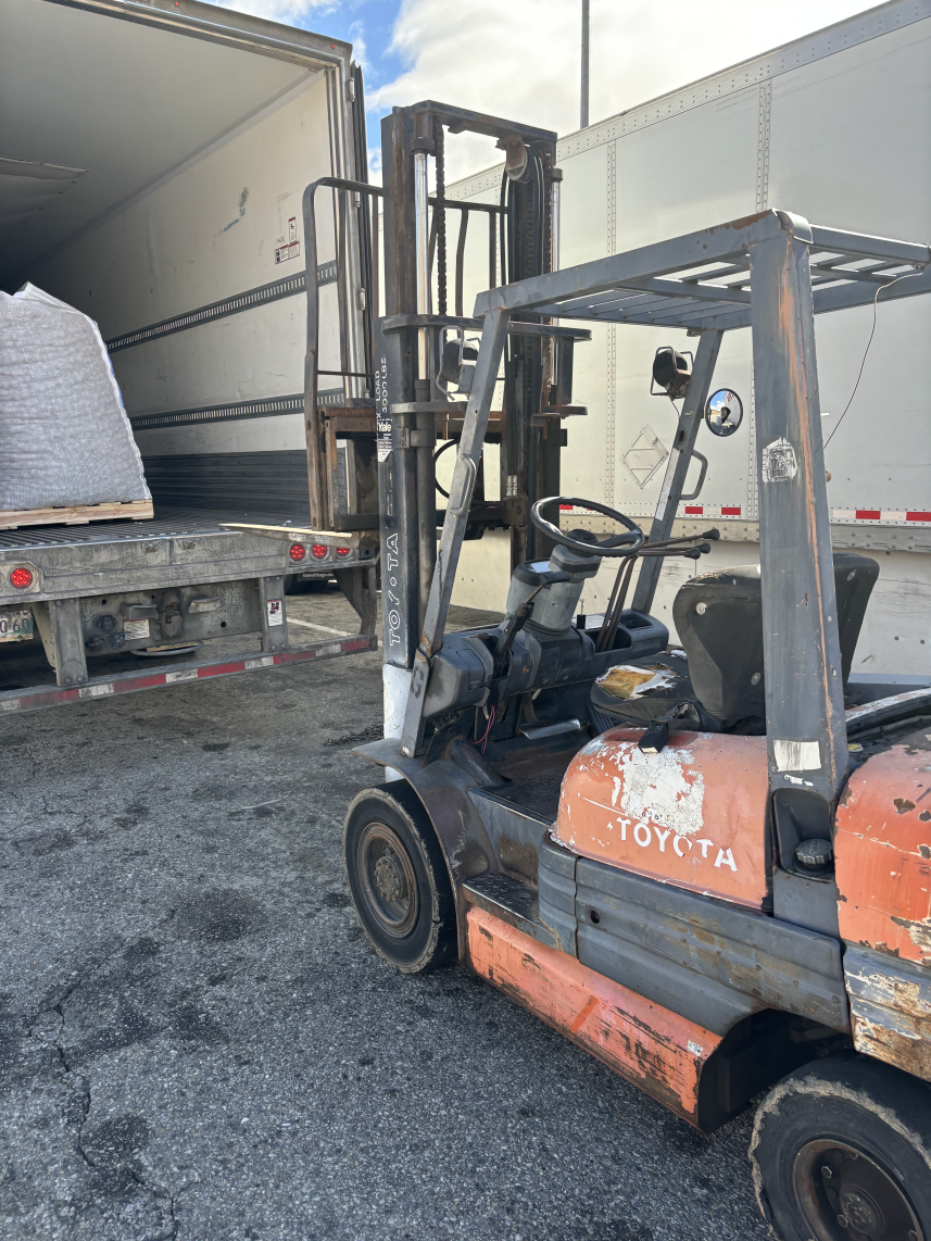Forklift loading cargo into a semi-truck trailer outdoors on a cloudy day.