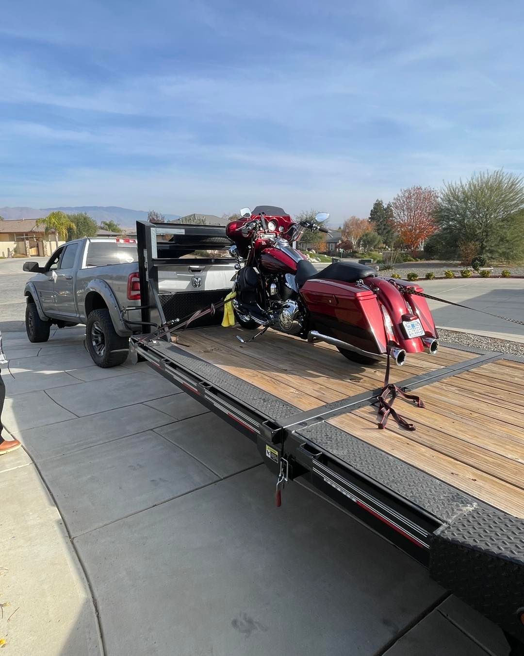 A red motorcycle on a flatbed trailer towed by a gray pickup truck. Outdoors.