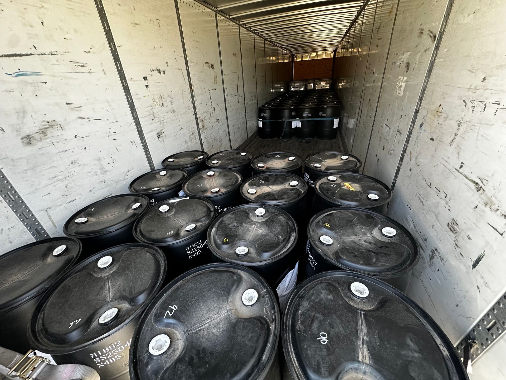 Inside of a truck trailer filled with black barrels.