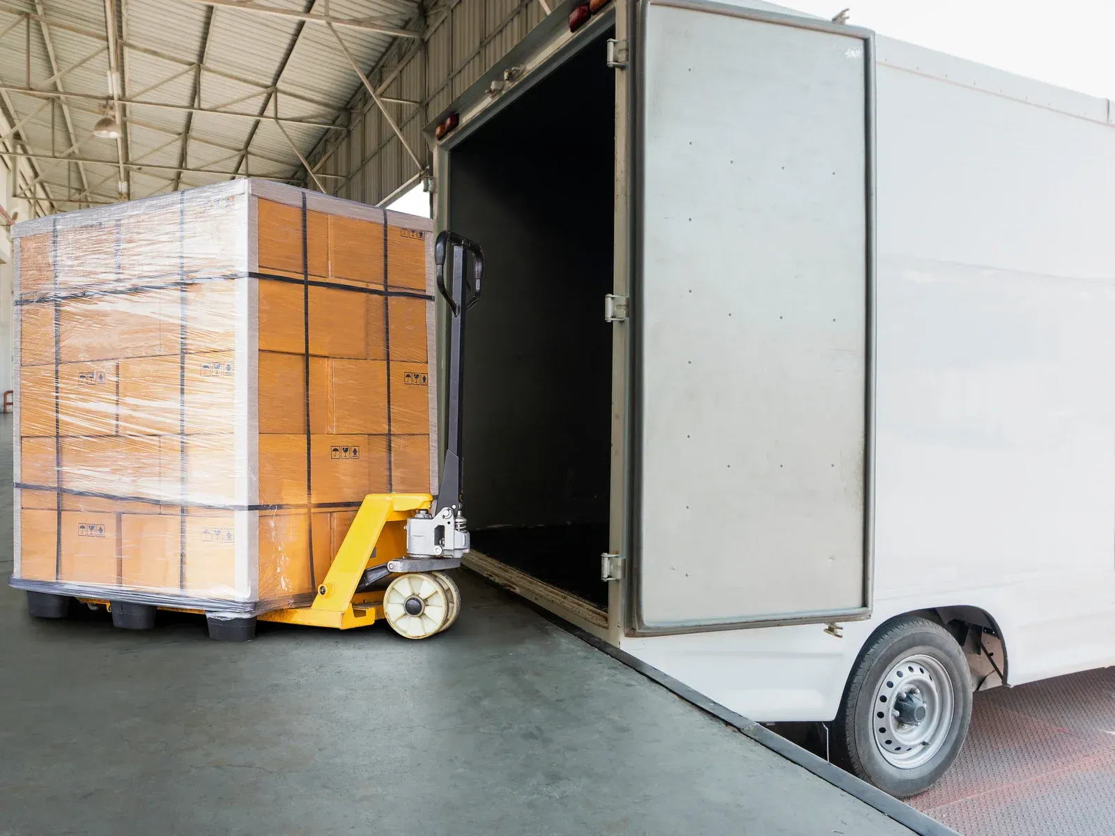 Pallet of boxes on a forklift being loaded into a white delivery truck at a loading dock.