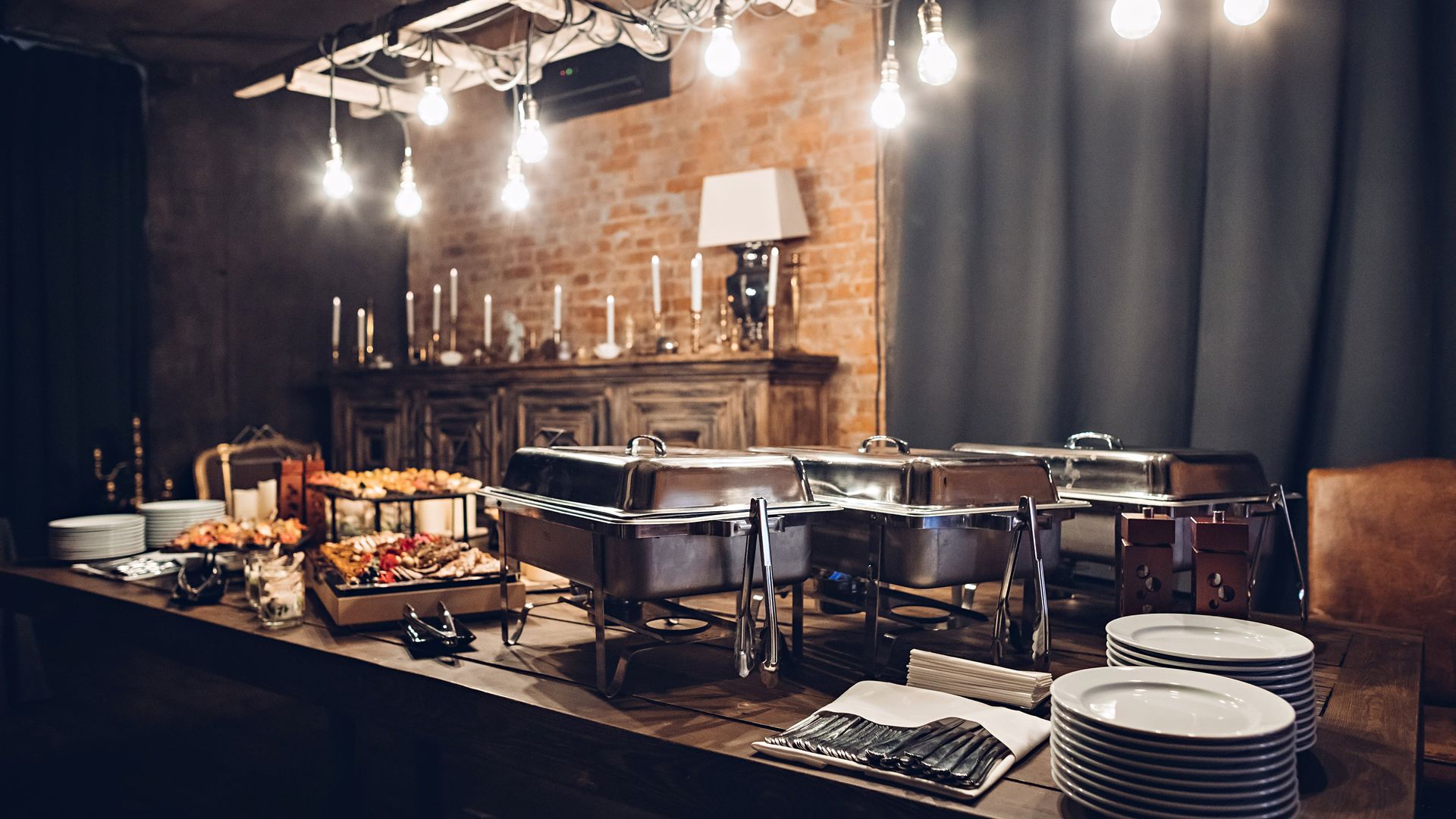 Buffet table with various food dishes, warm lighting, and a brick wall backdrop.