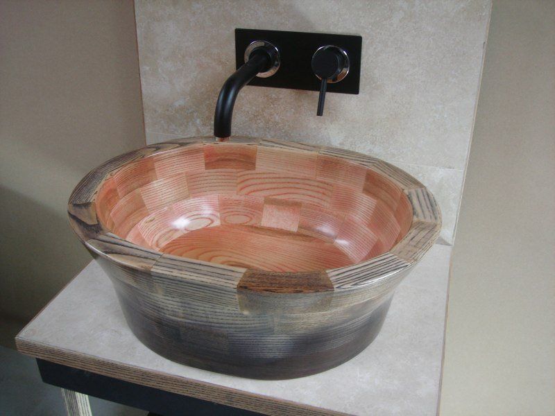 A wooden sink is sitting on a counter next to a wall mounted faucet