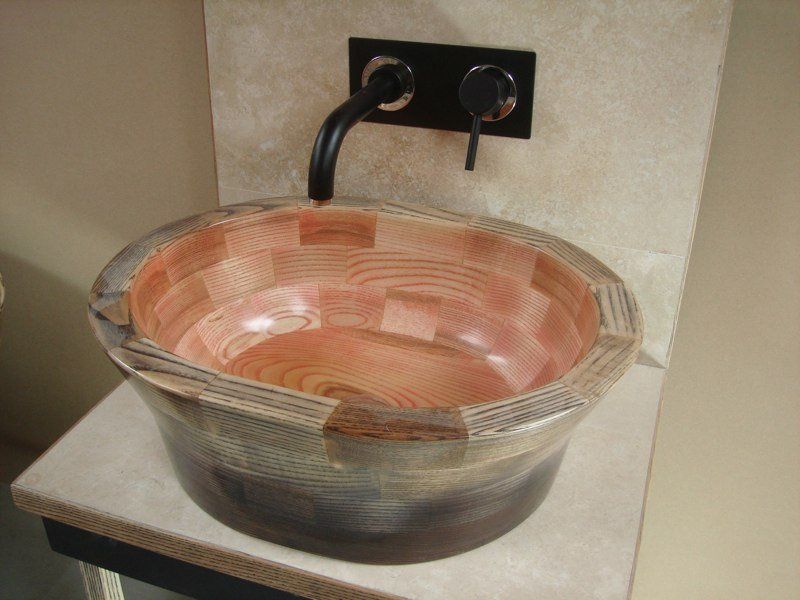 A wooden sink sits on a counter next to a wall mounted faucet