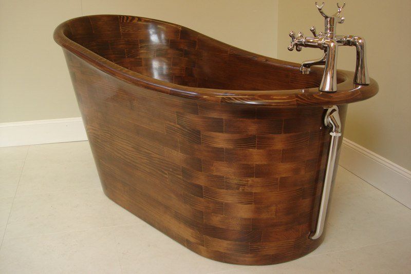 A wooden bathtub with chrome faucets in a bathroom
