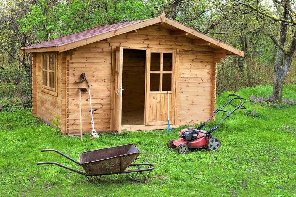 Wooden Shed With Open Door on Green Grass, Next to a Lawnmower and Wheelbarrow — ShedBoss in Tolga, QLD