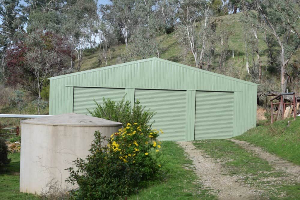 Green Metal Shed With Three Garage Doors, Dirt Driveway — ShedBoss in Mareeba, QLD