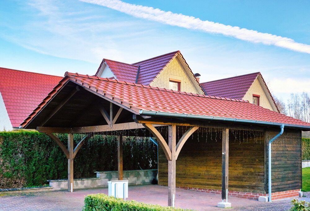 Carport With Dark Wood Frame and Red Tile Roof, Next to a House With Matching Roof — ShedBoss in Malanda, QLD