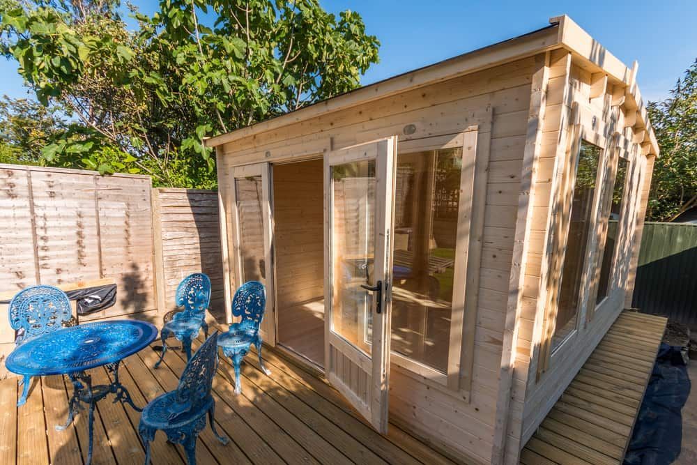 Wooden Cabin With Glass Doors and Windows, Deck, and Blue Patio Furniture in a Sunny Backyard — ShedBoss in Malanda, QLD
