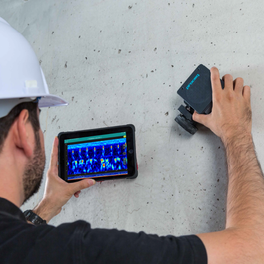 Construction worker using device on wall, viewing display on tablet.