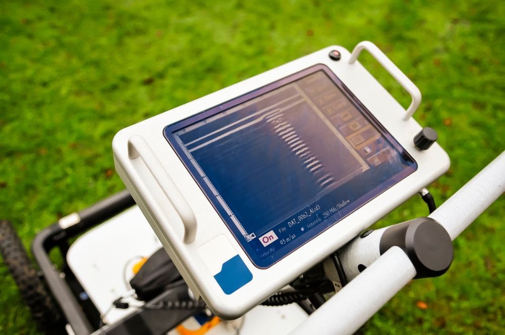 A close-up view of a ground-penetrating radar display screen mounted on a cart, set against a green grass background.