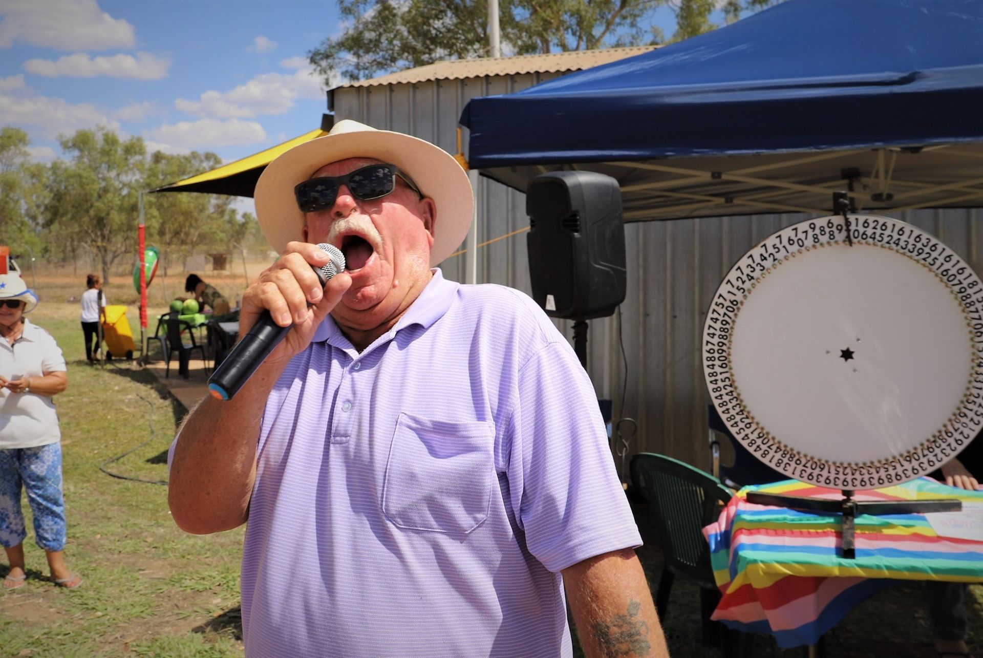 A man in a hat and sunglasses is singing into a microphone.