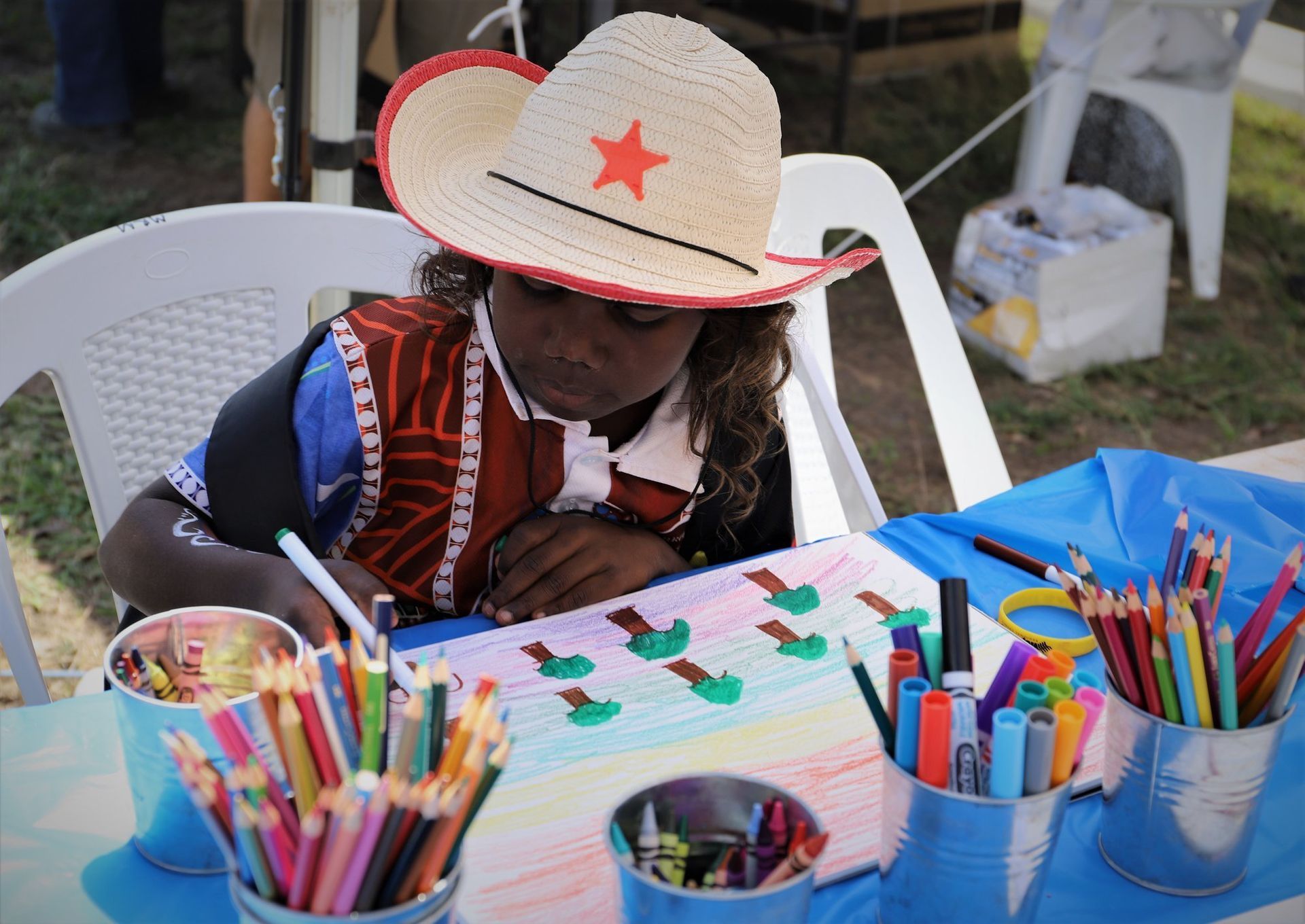 A child wearing a cowboy hat is drawing on a piece of paper