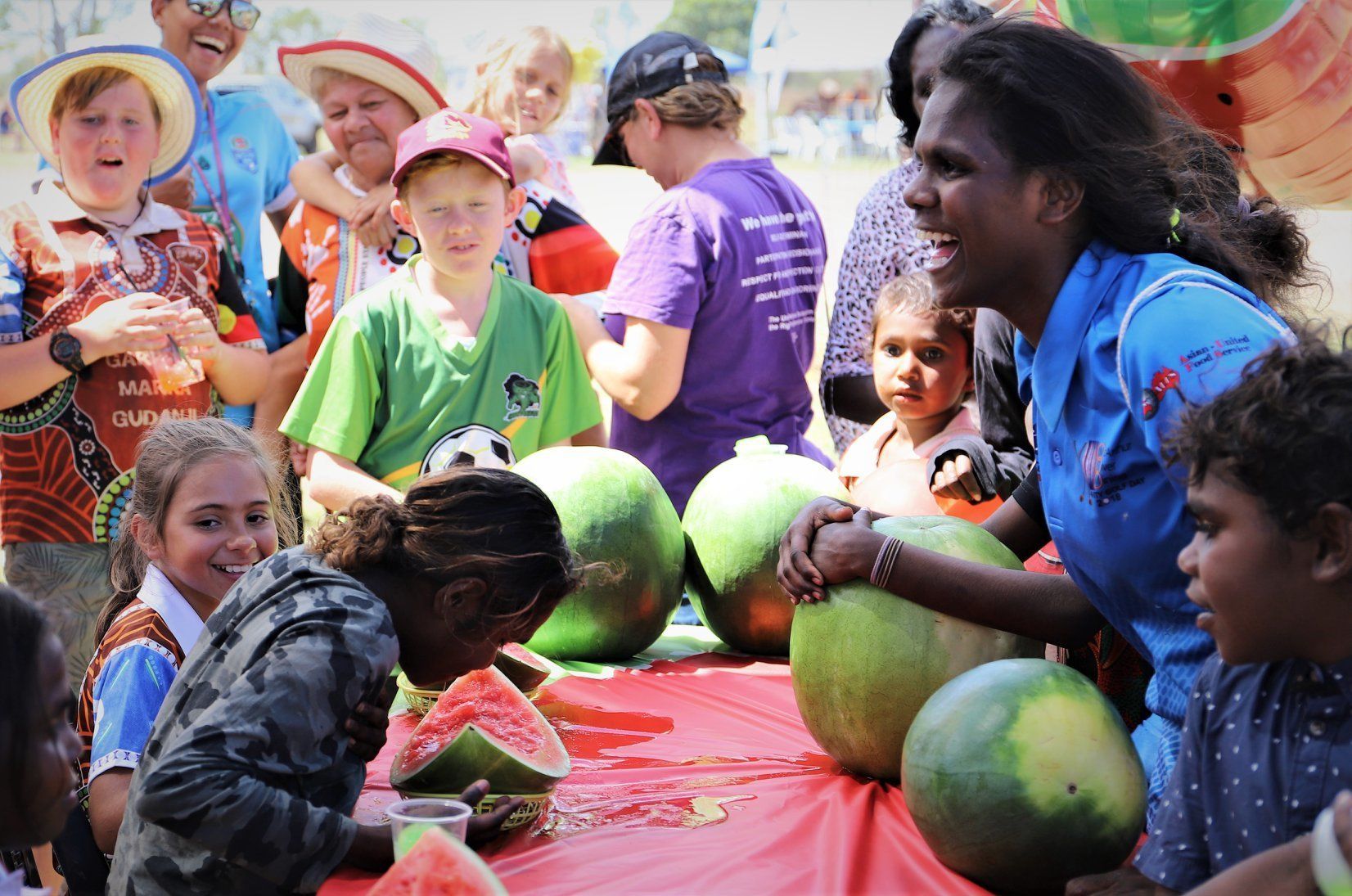 A group of people are sitting around a table with watermelons.