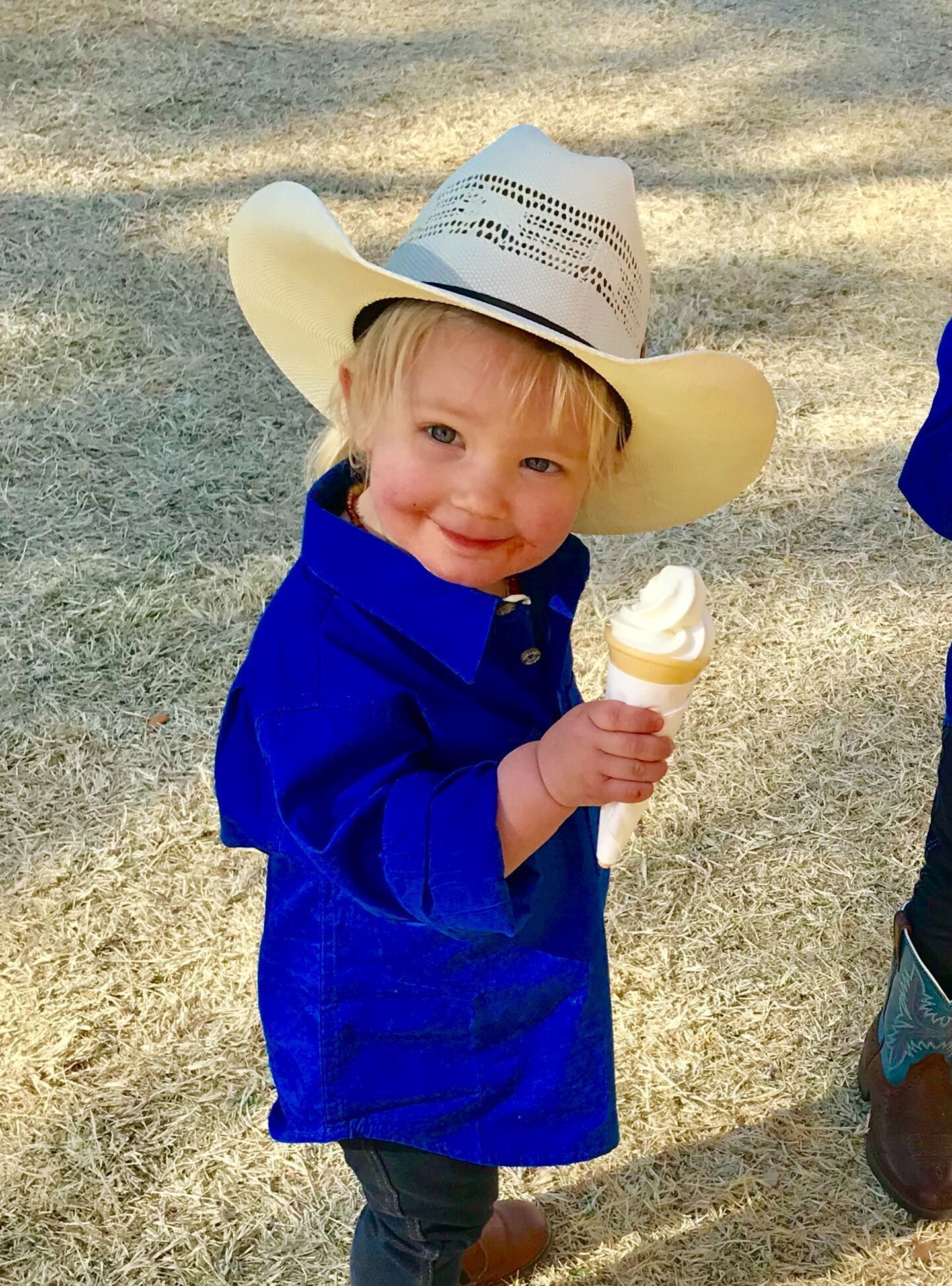 A little boy wearing a cowboy hat is holding an ice cream cone.