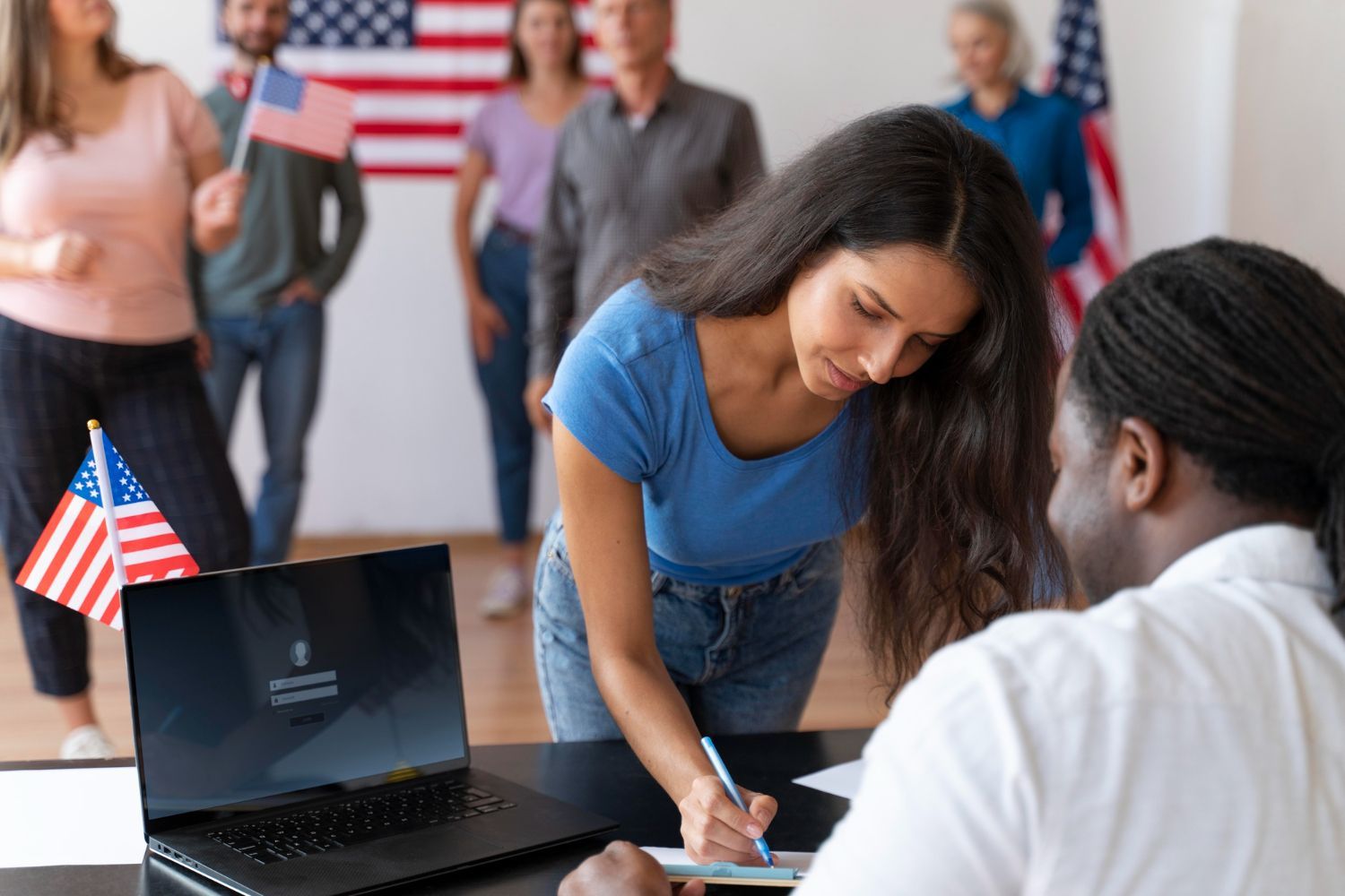 A man and a woman are signing a document in front of an american flag.