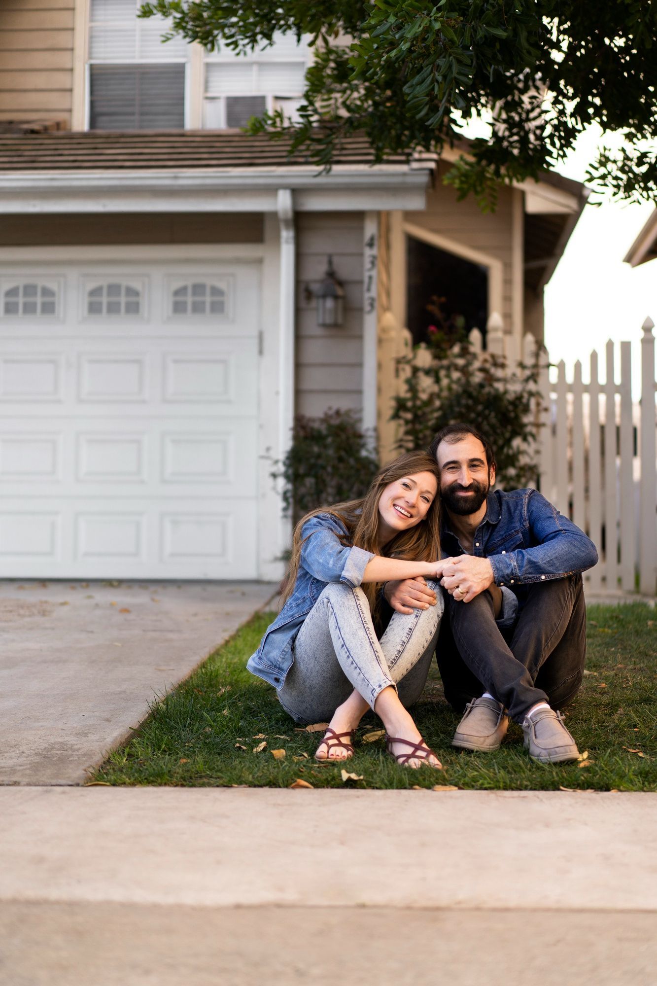 A man and a woman are sitting on the grass in front of a house.