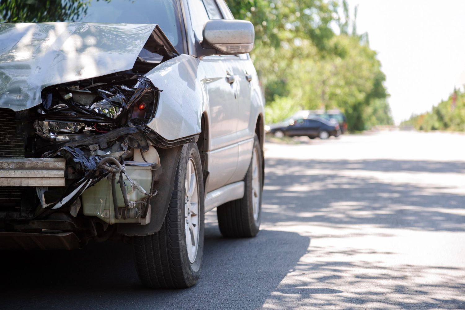 A car with a damaged front end is parked on the side of the road.