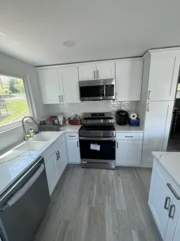 A kitchen with white cabinets , stainless steel appliances , a sink , and a window.