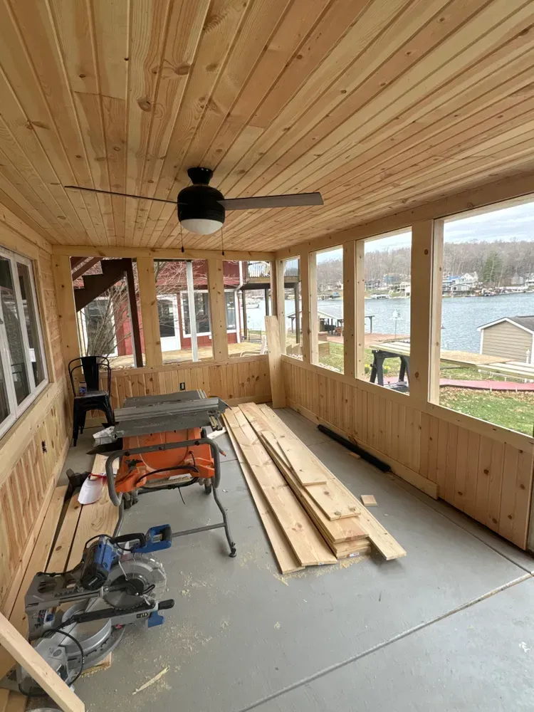 A wooden porch with a table and a ceiling fan.