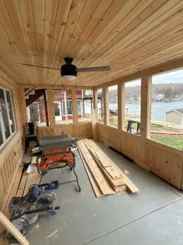 A wooden porch with a table and a ceiling fan.