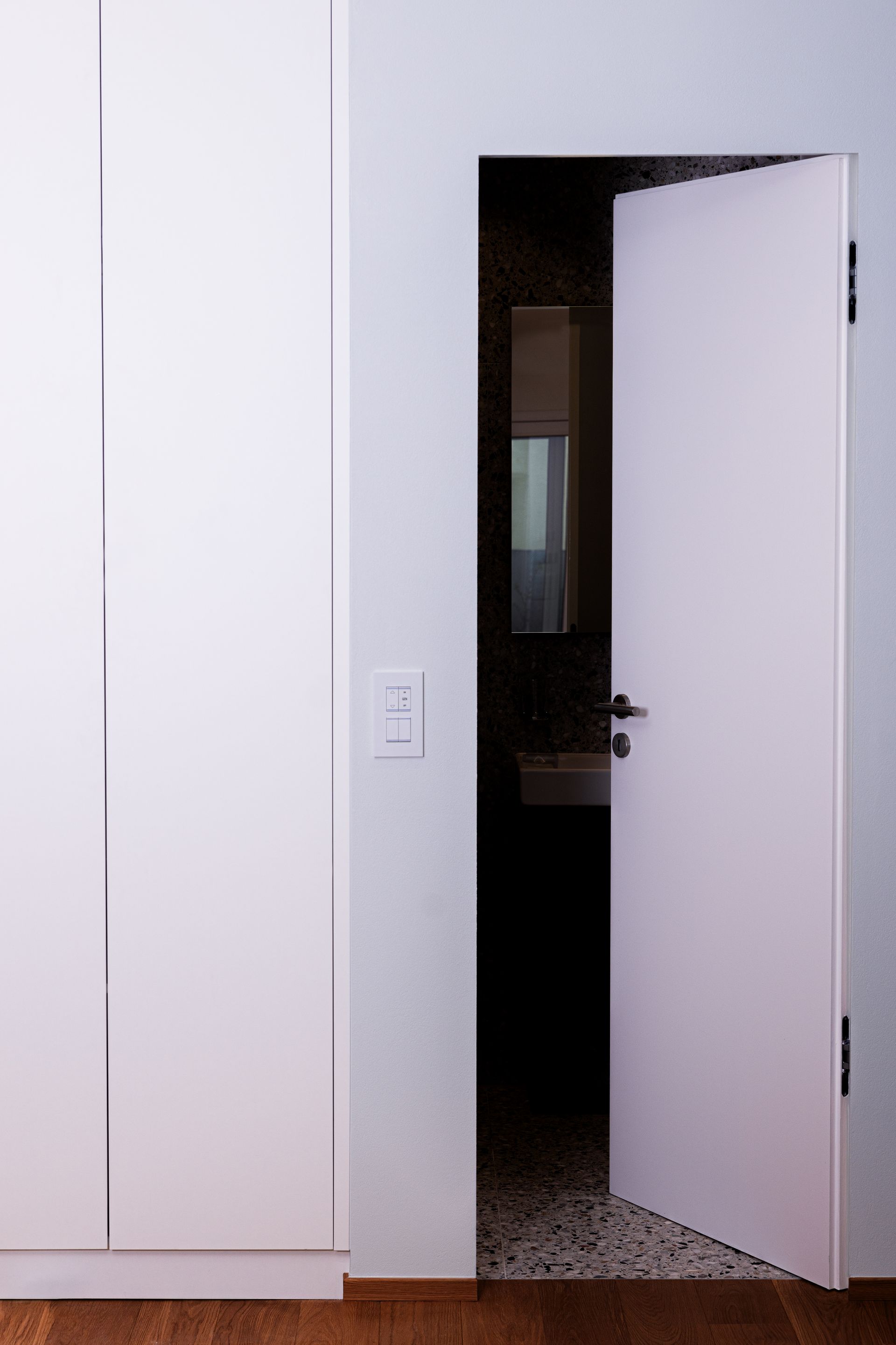 Une porte blanche est ouverte sur une salle de bain avec lavabo.