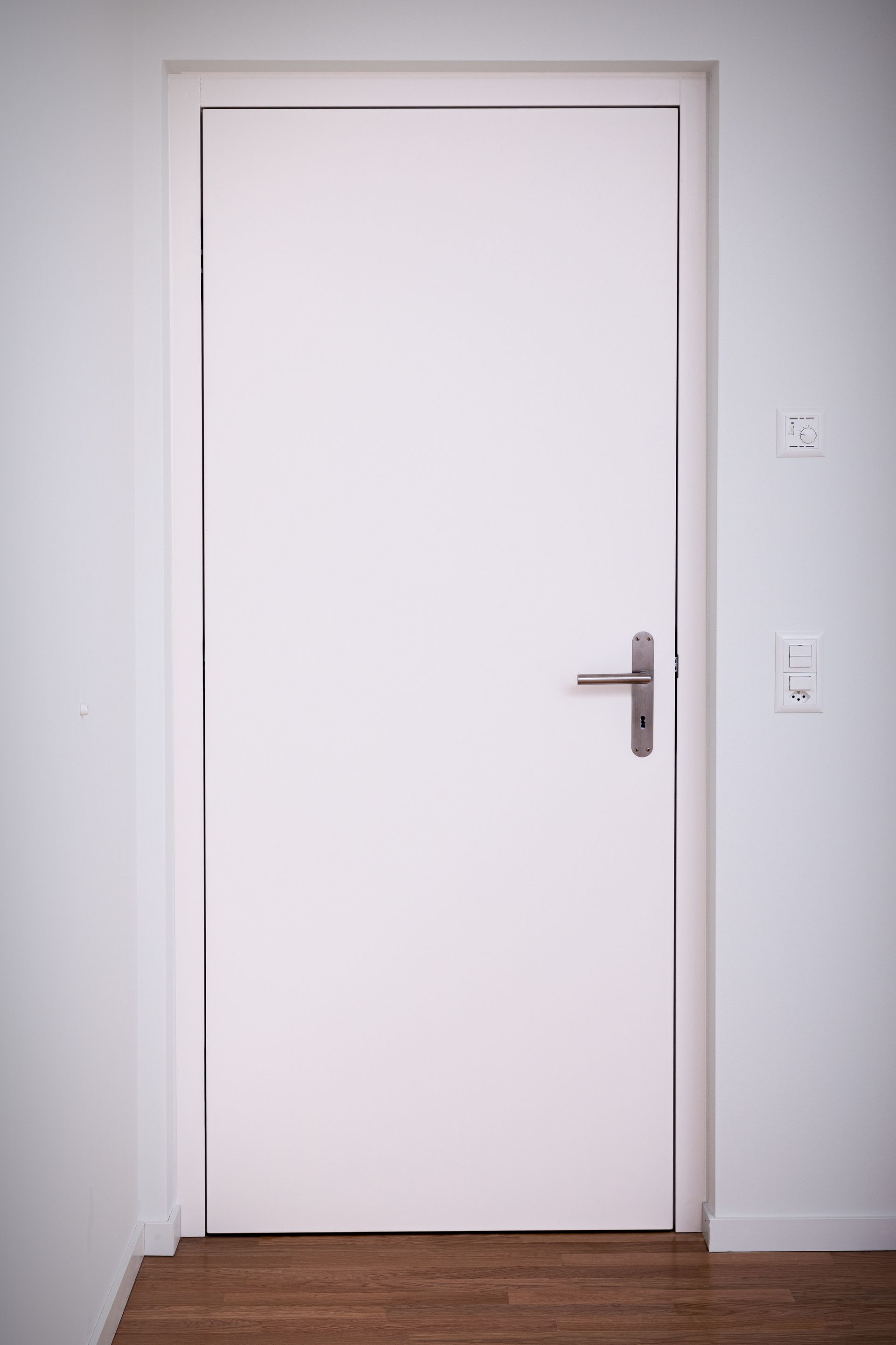 Une porte blanche avec une poignée en métal se trouve dans une pièce avec un parquet en bois.