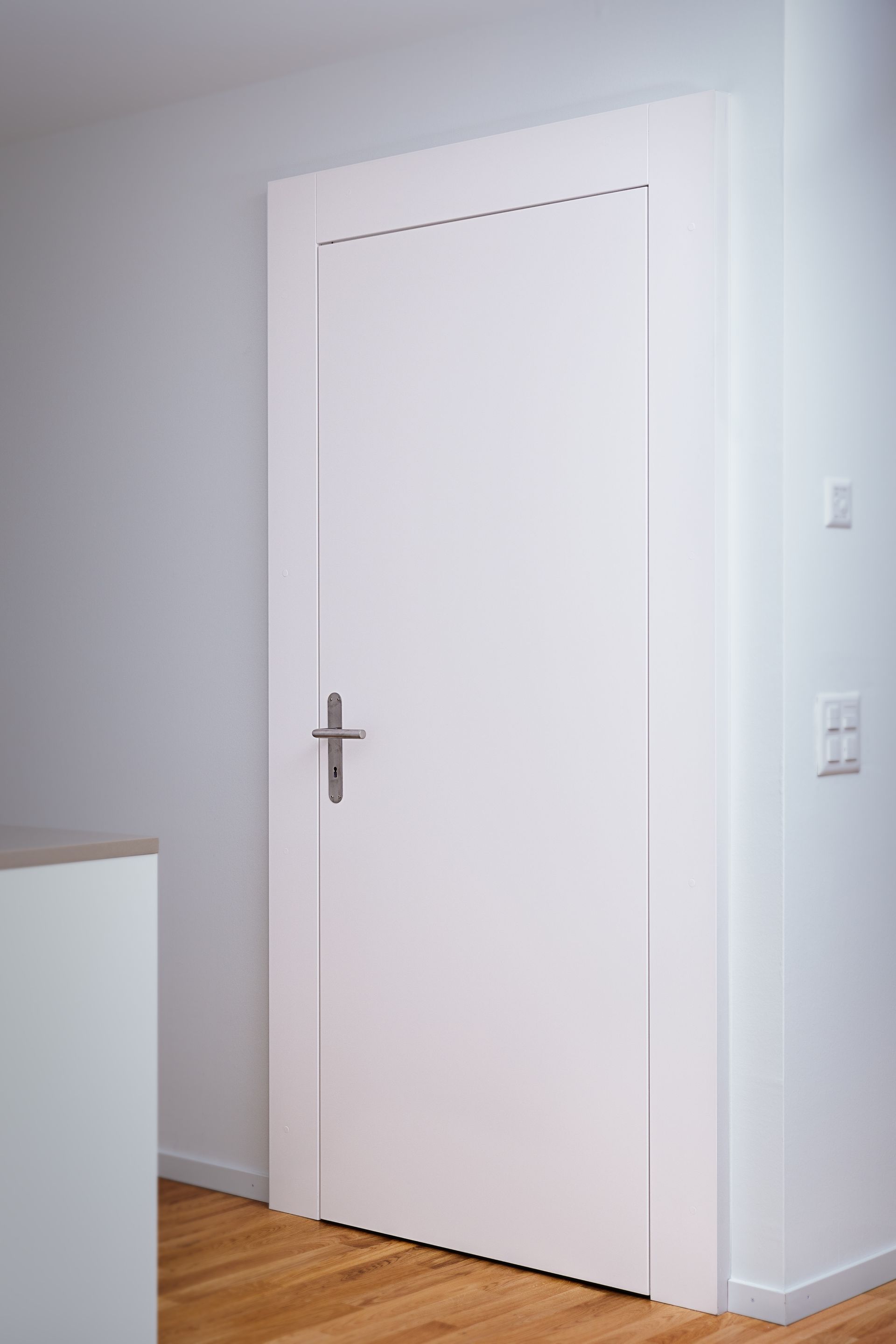 Une porte blanche se trouve dans un coin d'une pièce à côté d'un parquet.