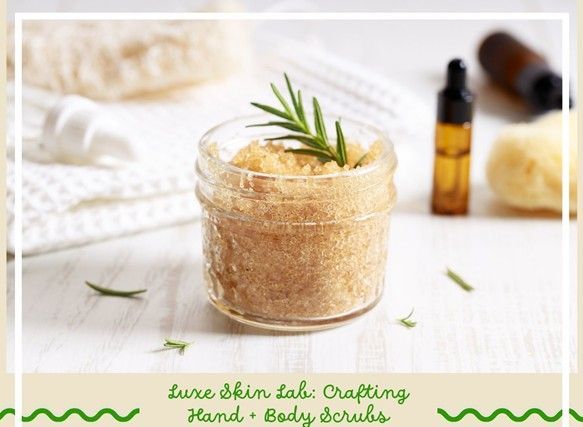 A jar of brown sugar scrub topped with a rosemary sprig, set on a white table with essential oil and towels.