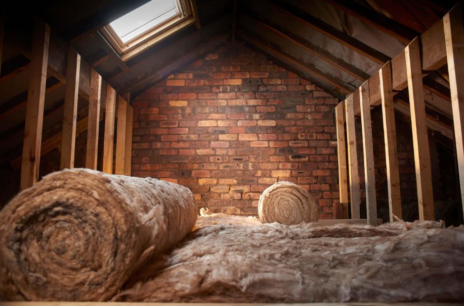 Loft with rolled insulation and exposed brick wall, lit by a skylight.