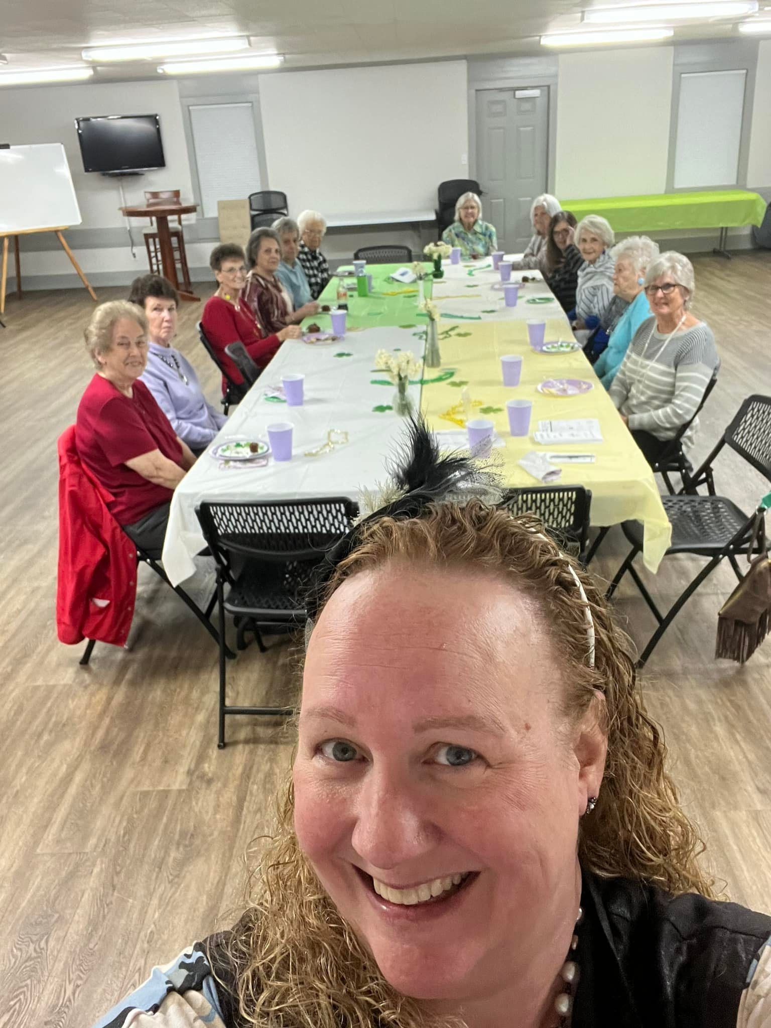 Woman takes selfie with a group of women at a decorated table in a room.