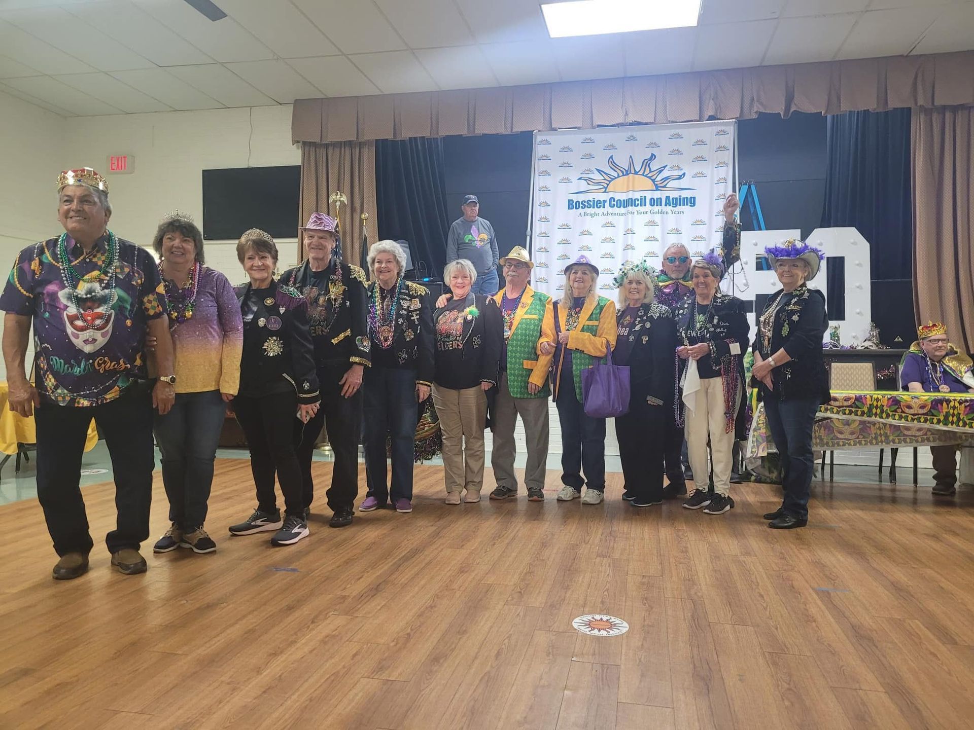 Group of people in Mardi Gras attire posing on a dance floor.